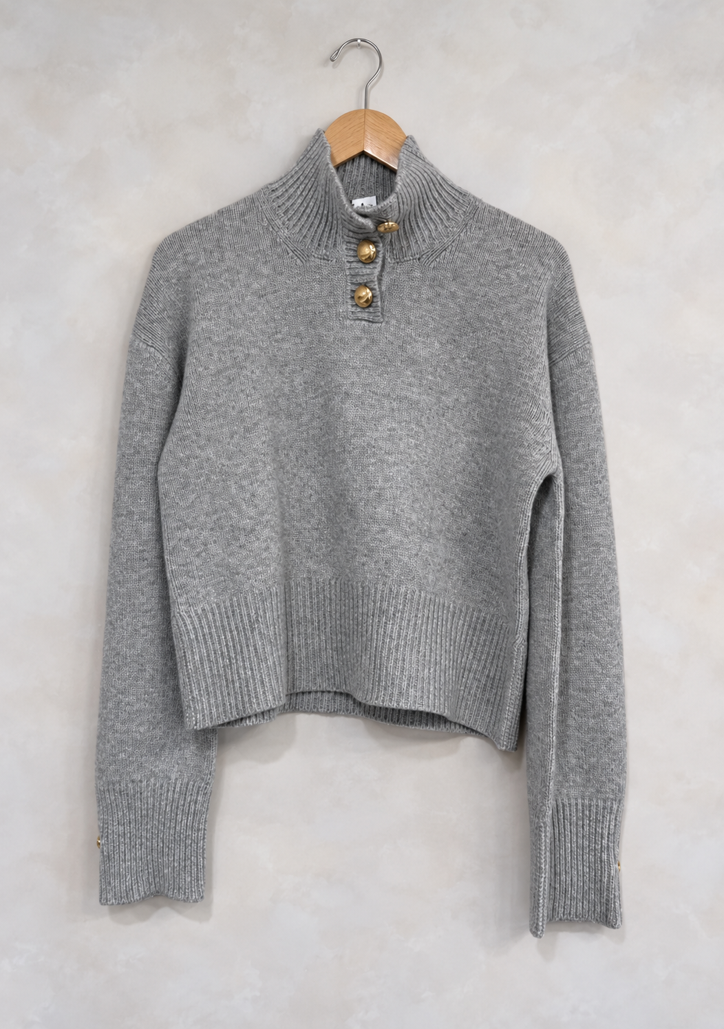 Sweater on wooden hanger against light gray plaster wall