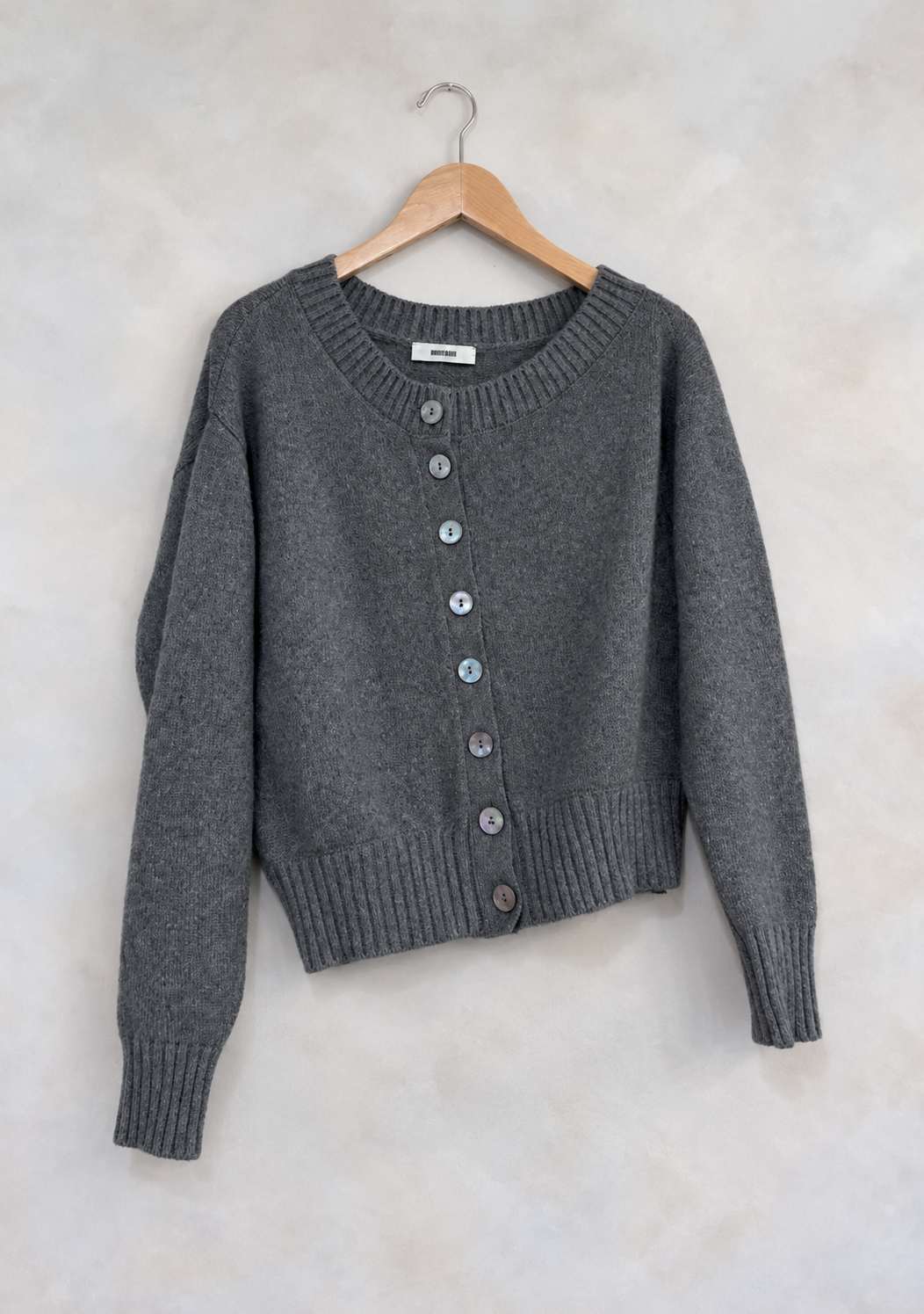 Sweater on wooden hanger against light gray plaster wall