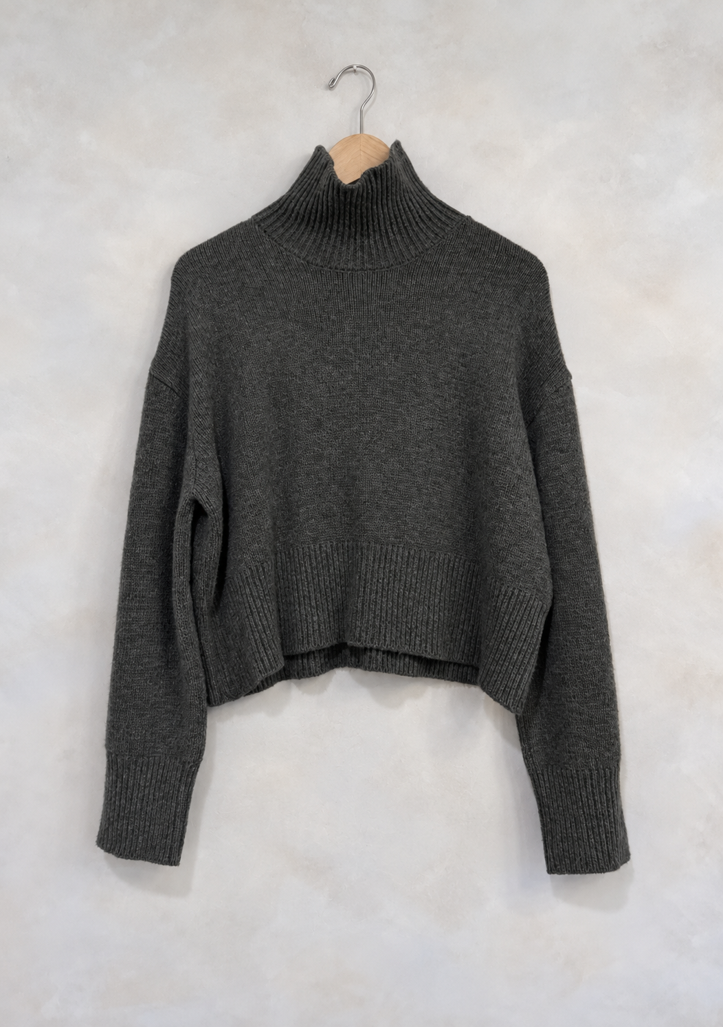 Sweater on wooden hanger against light gray plaster wall
