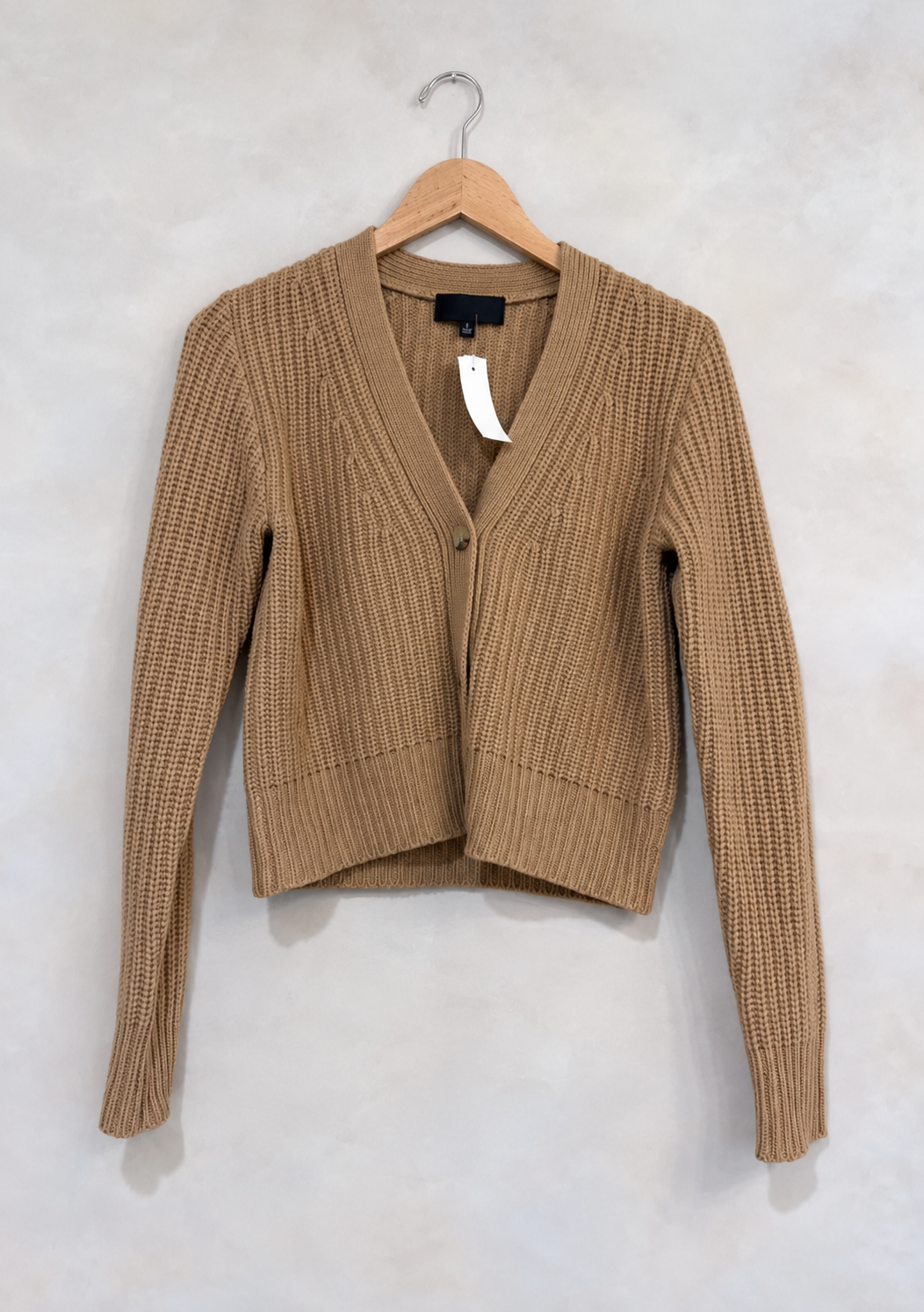 Sweater on wooden hanger against light gray plaster wall