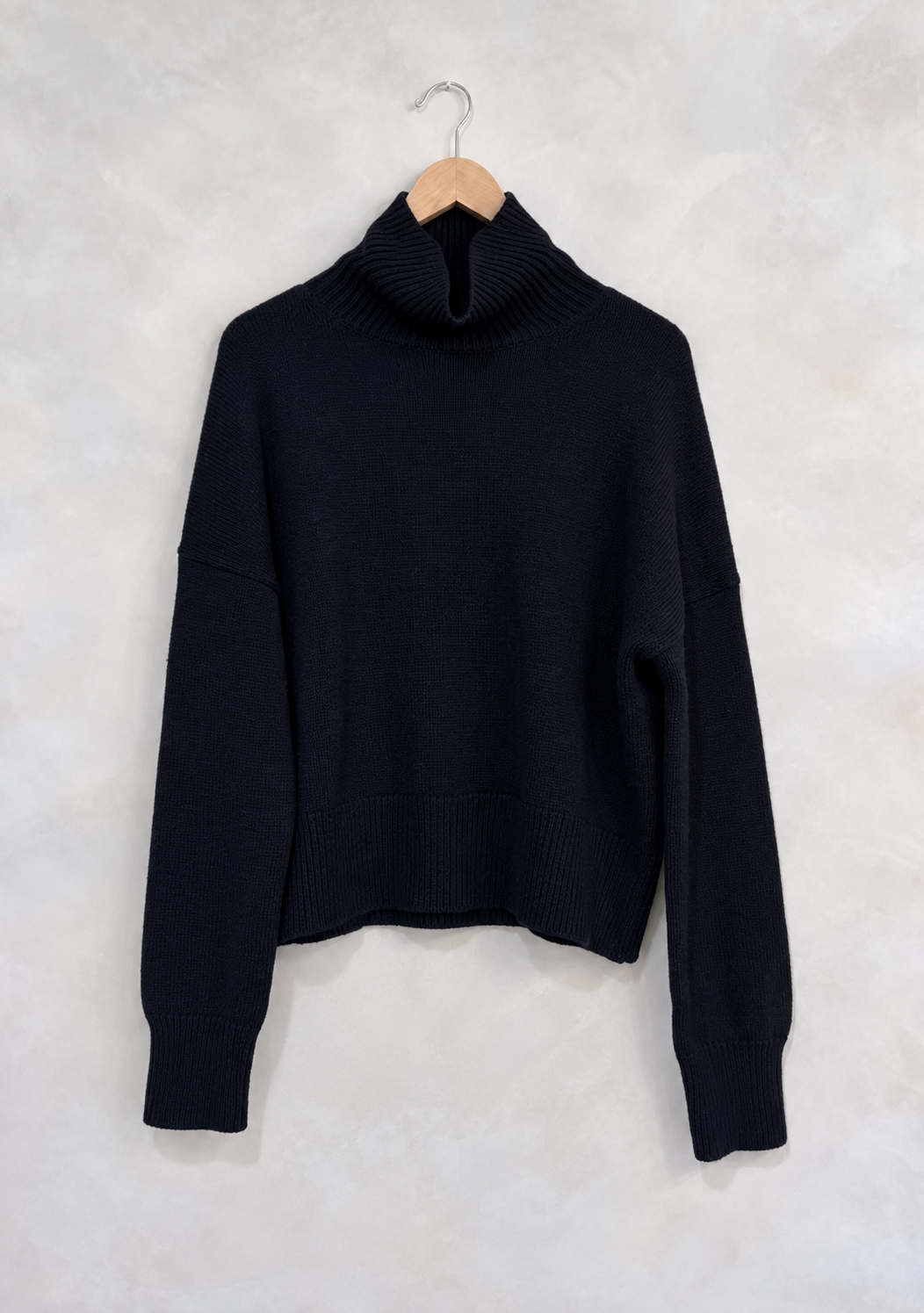 Sweater on wooden hanger against light gray plaster wall