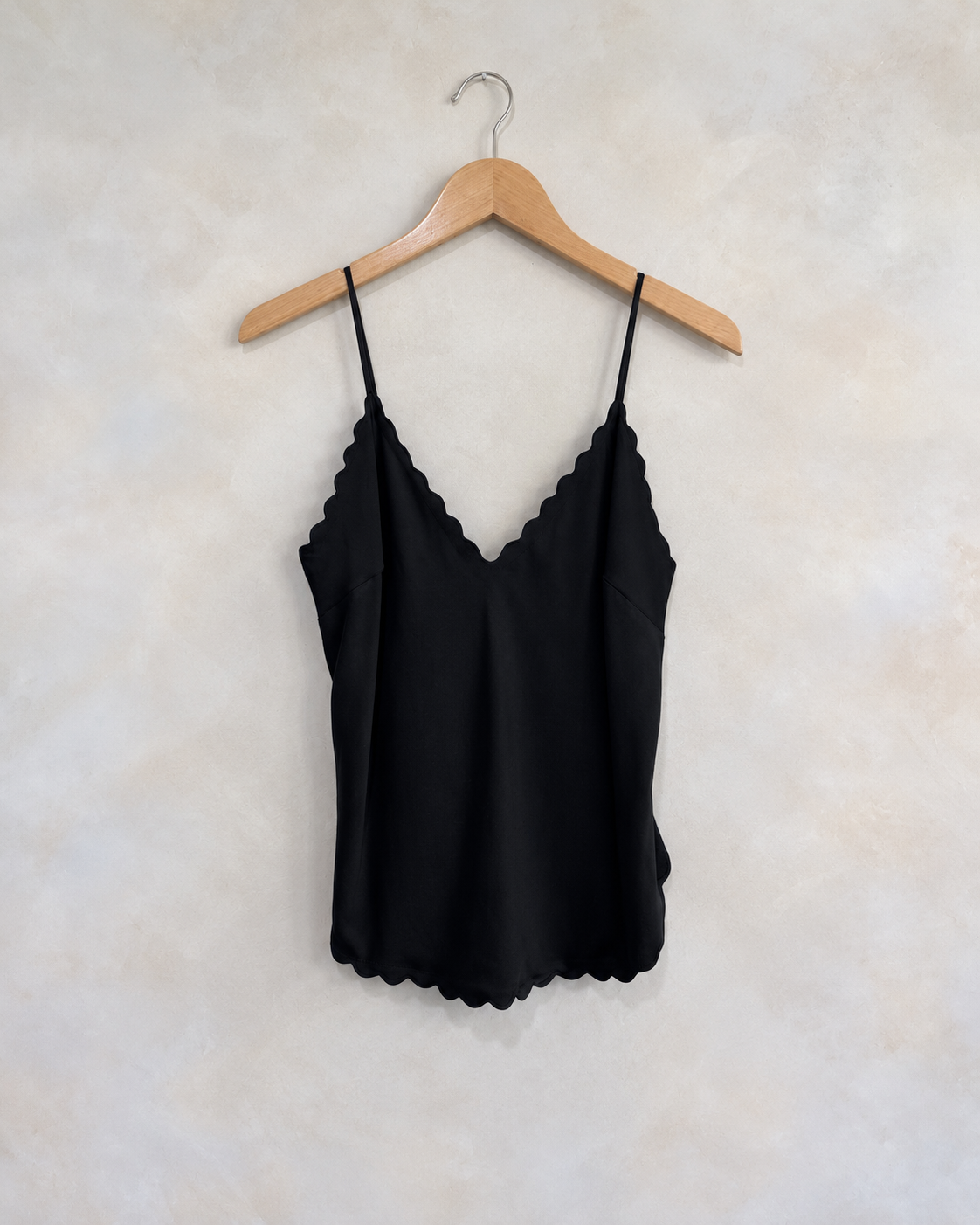 A.L.C black scalloped tank on a wooden hanger against a softly mottled pale wall