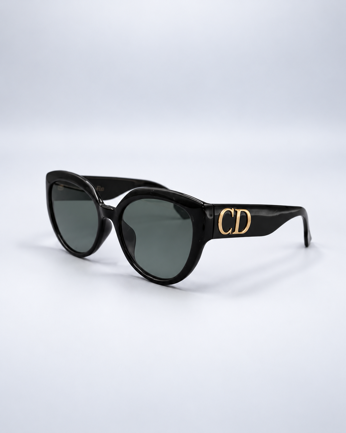 Christian Dior black sunglasses with gold CD detail on a pale gray studio background