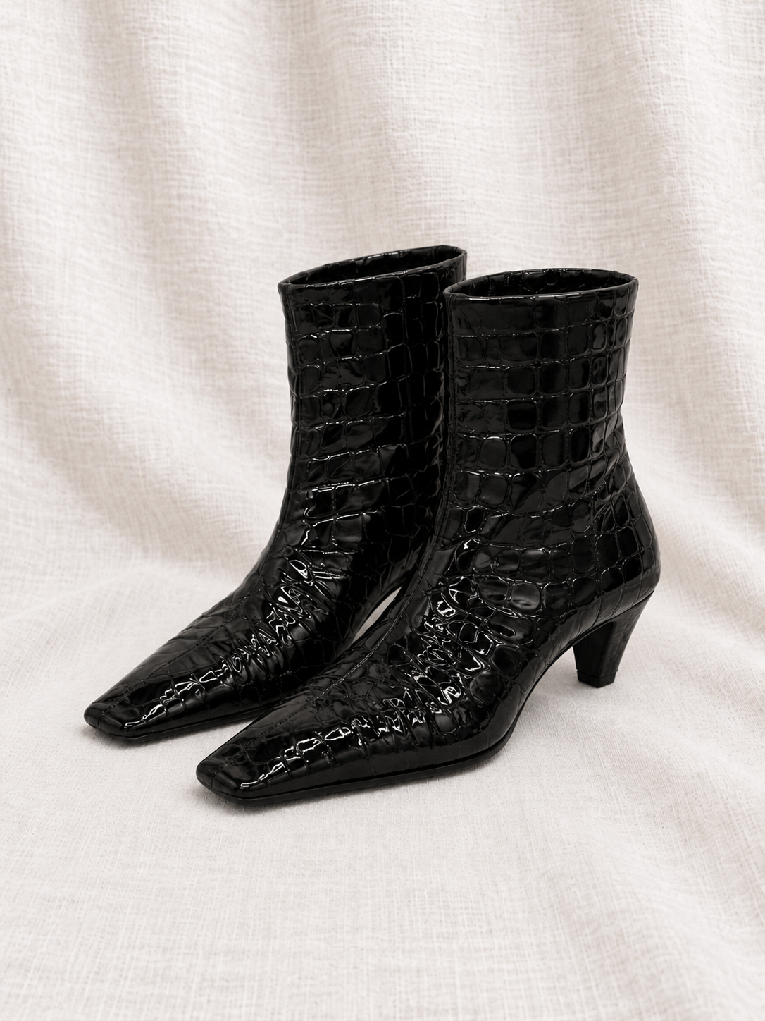 KHAITE Arizona black embossed ankle boots close together, facing left on ivory fabric
