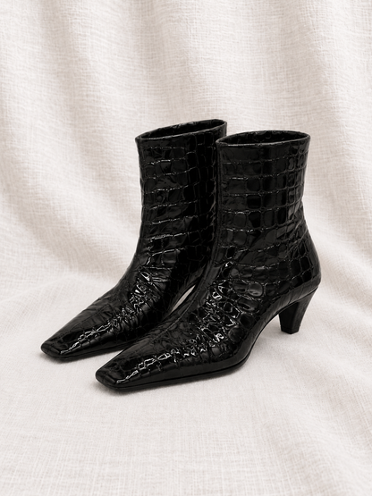 KHAITE Arizona black embossed ankle boots close together, facing left on ivory fabric