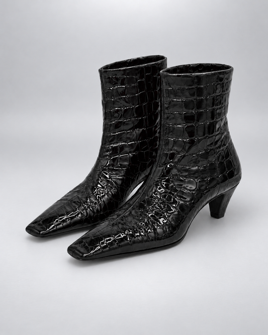 KHAITE Arizona black embossed ankle boots close together, facing left on ivory fabric