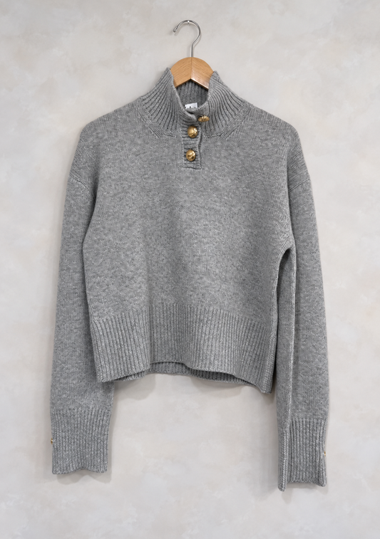 Sweater on wooden hanger against light gray plaster wall