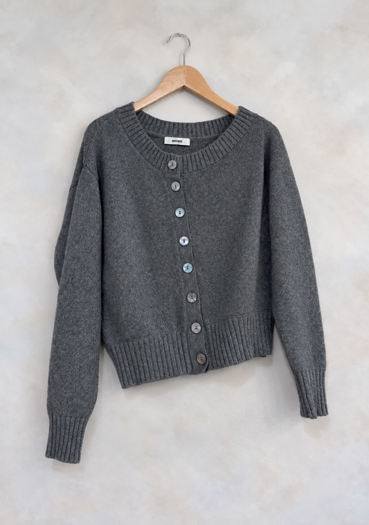 Sweater on wooden hanger against light gray plaster wall