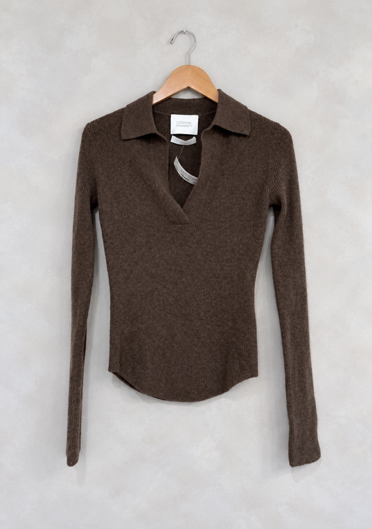 Sweater on wooden hanger against light gray plaster wall