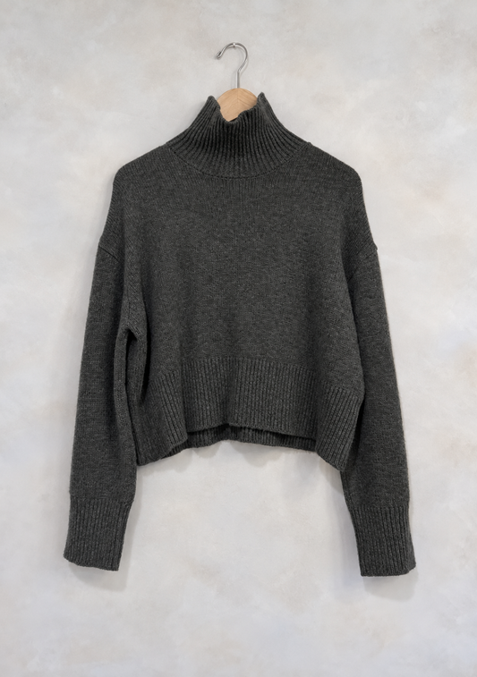 Sweater on wooden hanger against light gray plaster wall