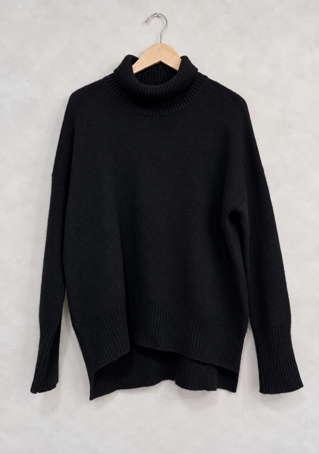 Sweater on wooden hanger against light gray plaster wall