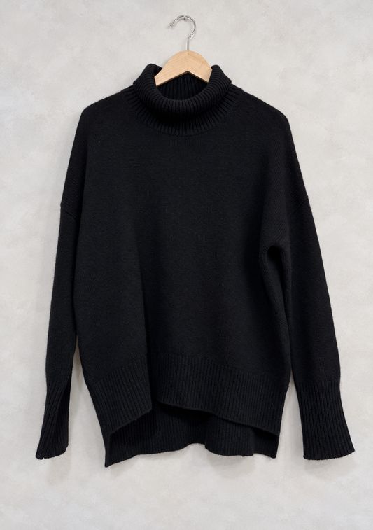 Sweater on wooden hanger against light gray plaster wall