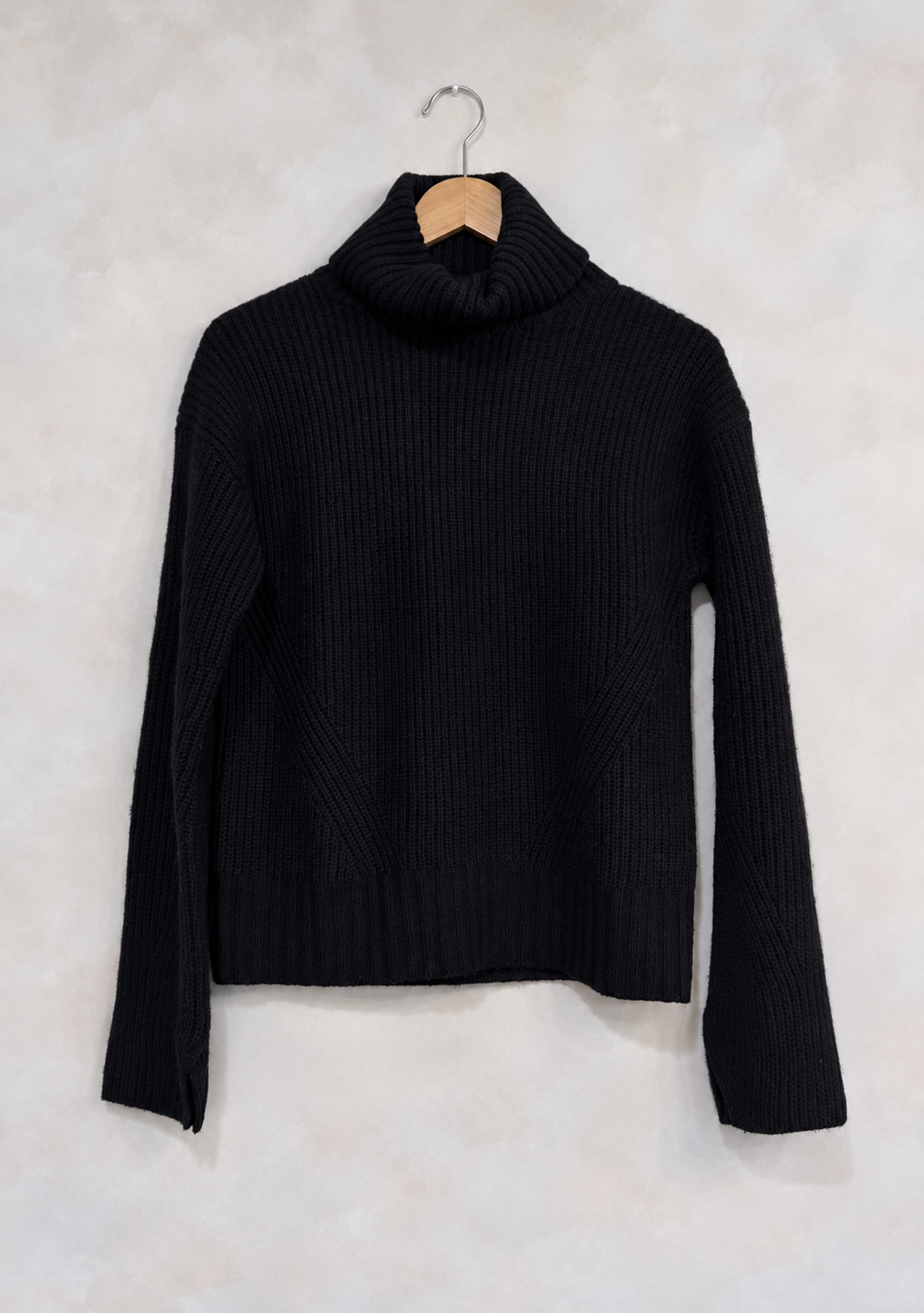 Sweater on wooden hanger against light gray plaster wall