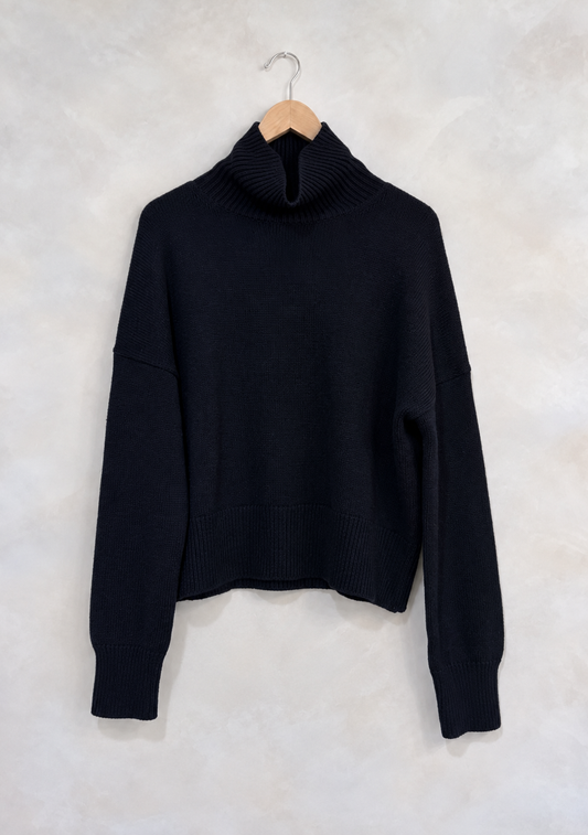 Sweater on wooden hanger against light gray plaster wall