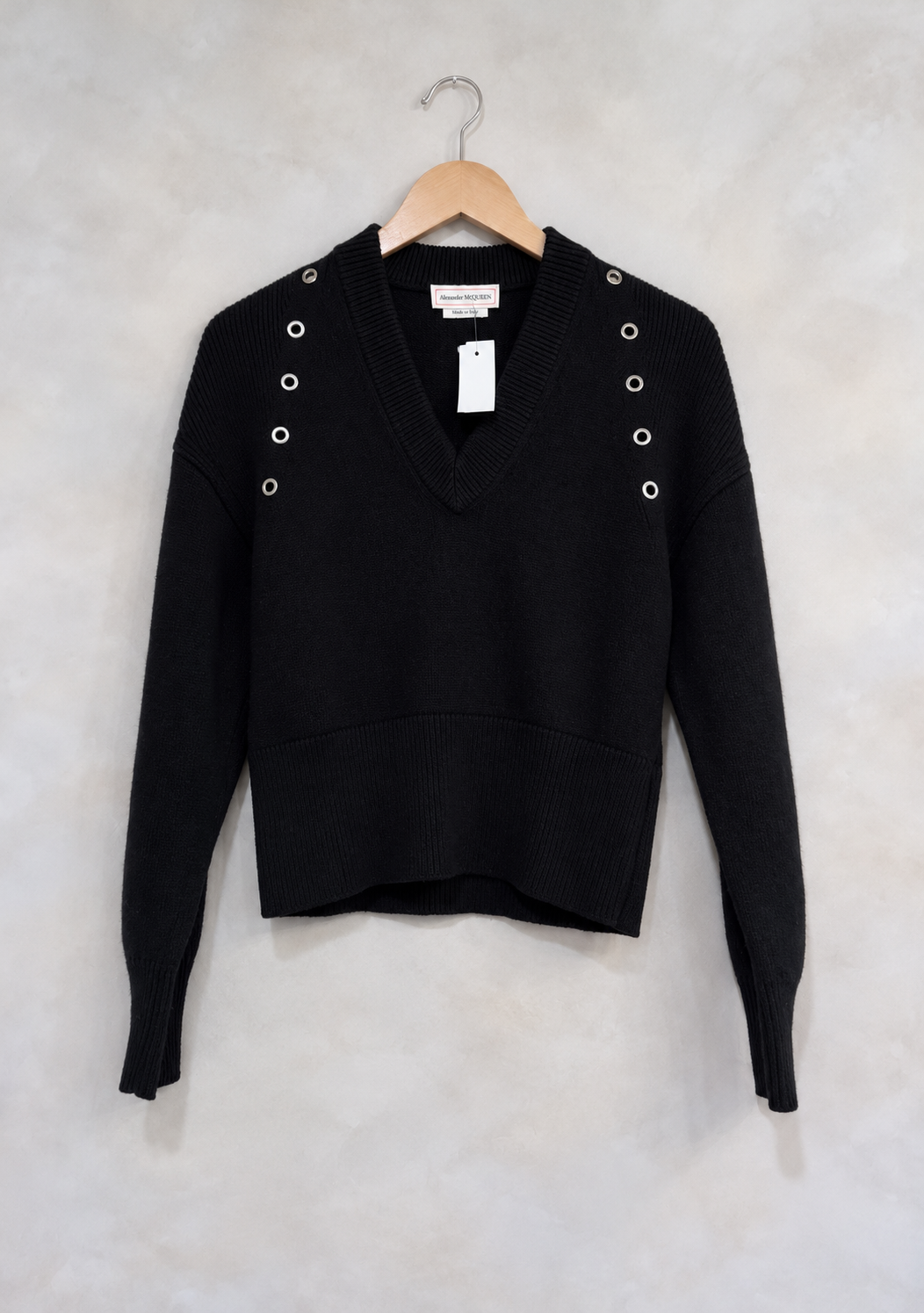 Sweater on wooden hanger against light gray plaster wall