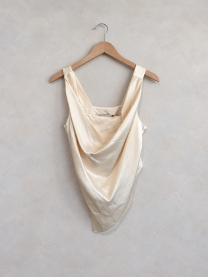 Nanushka ivory silk draped tank on a wooden hanger against a pale textured wall
