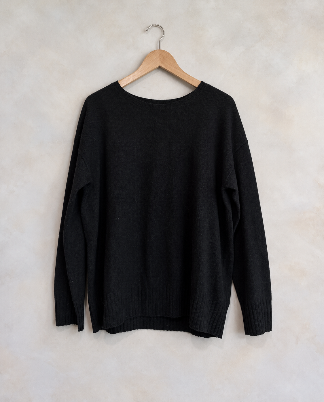 Garment on a wooden hanger against a pale textured wall