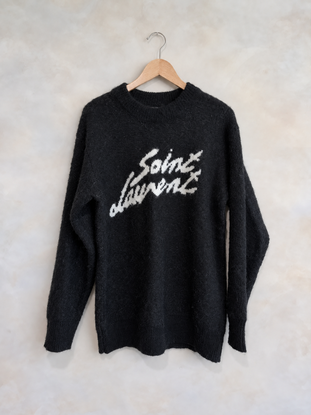 Saint Laurent black mohair crewneck sweater on a wooden hanger against a pale textured wall