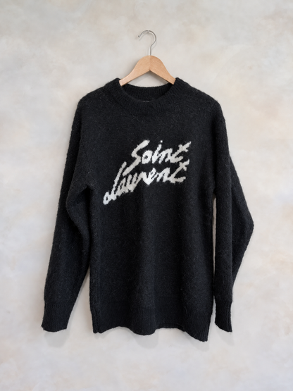Saint Laurent black mohair crewneck sweater on a wooden hanger against a pale textured wall
