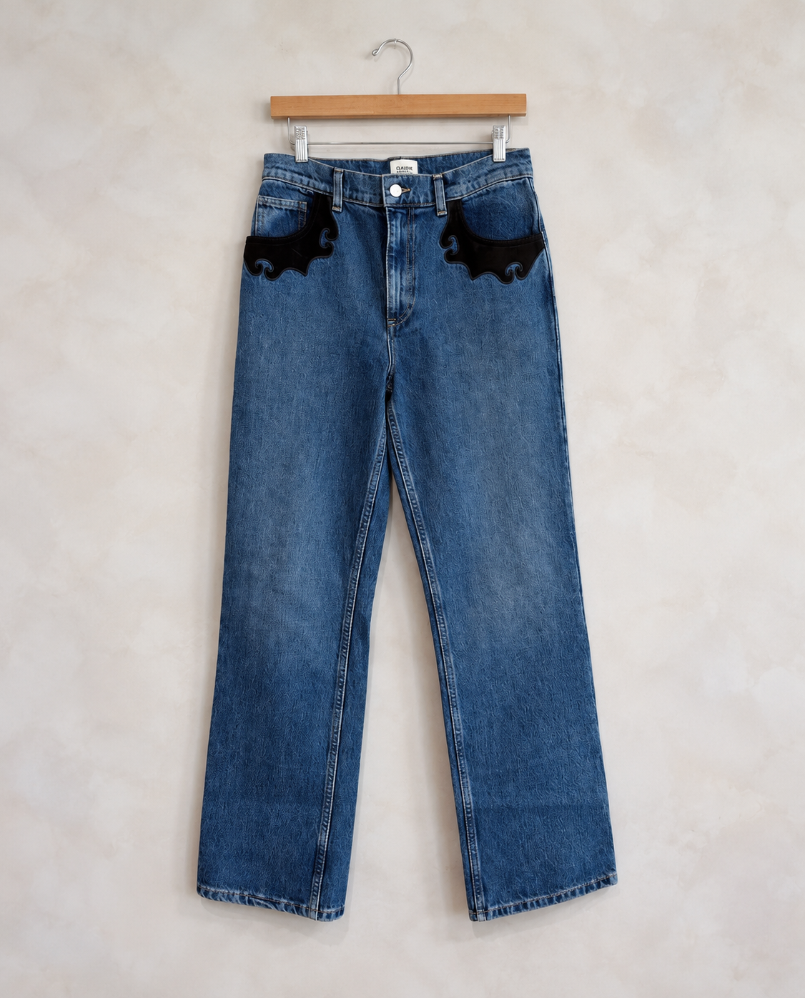 Garment on wooden hanger against pale textured wall