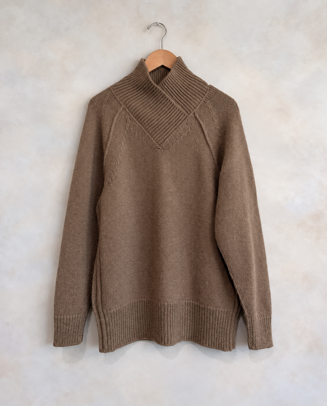 Garment on wooden hanger against pale textured wall