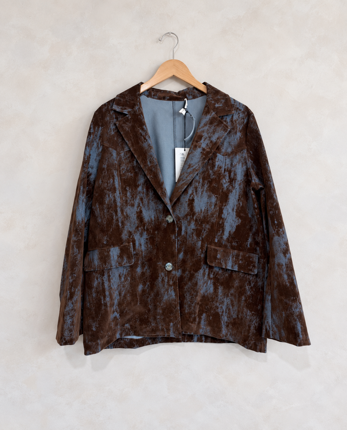Garment on wooden hanger against pale textured wall