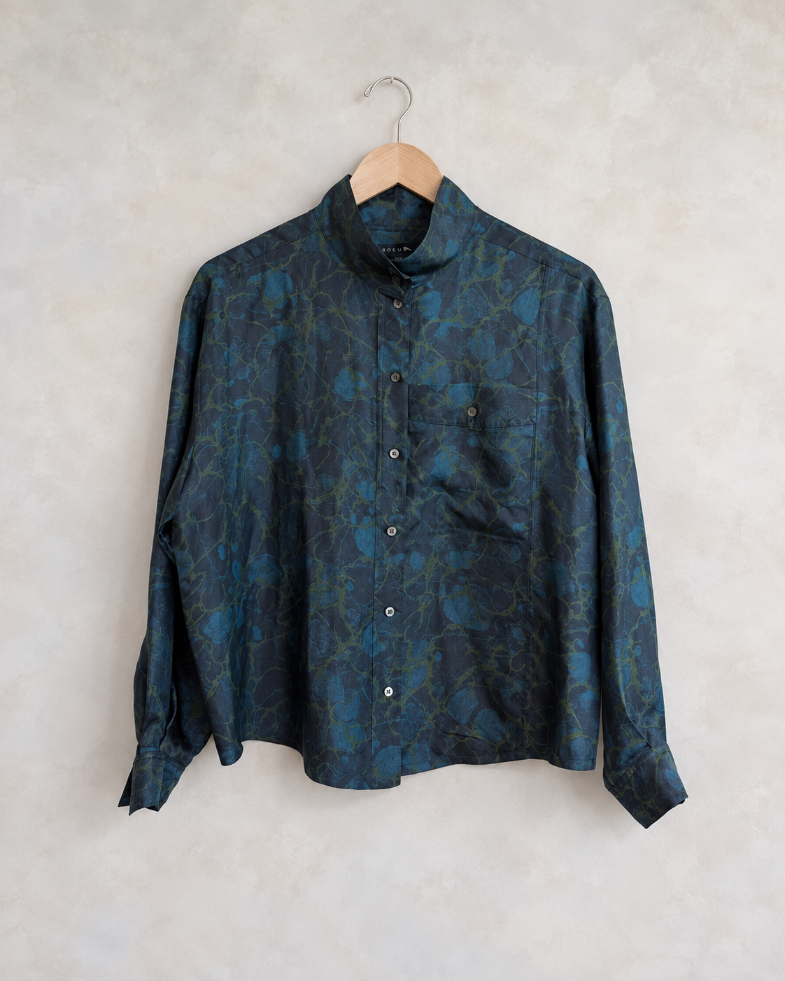 Soeur silk swirl print blouse photographed on a wooden hanger against a pale neutral textured wall