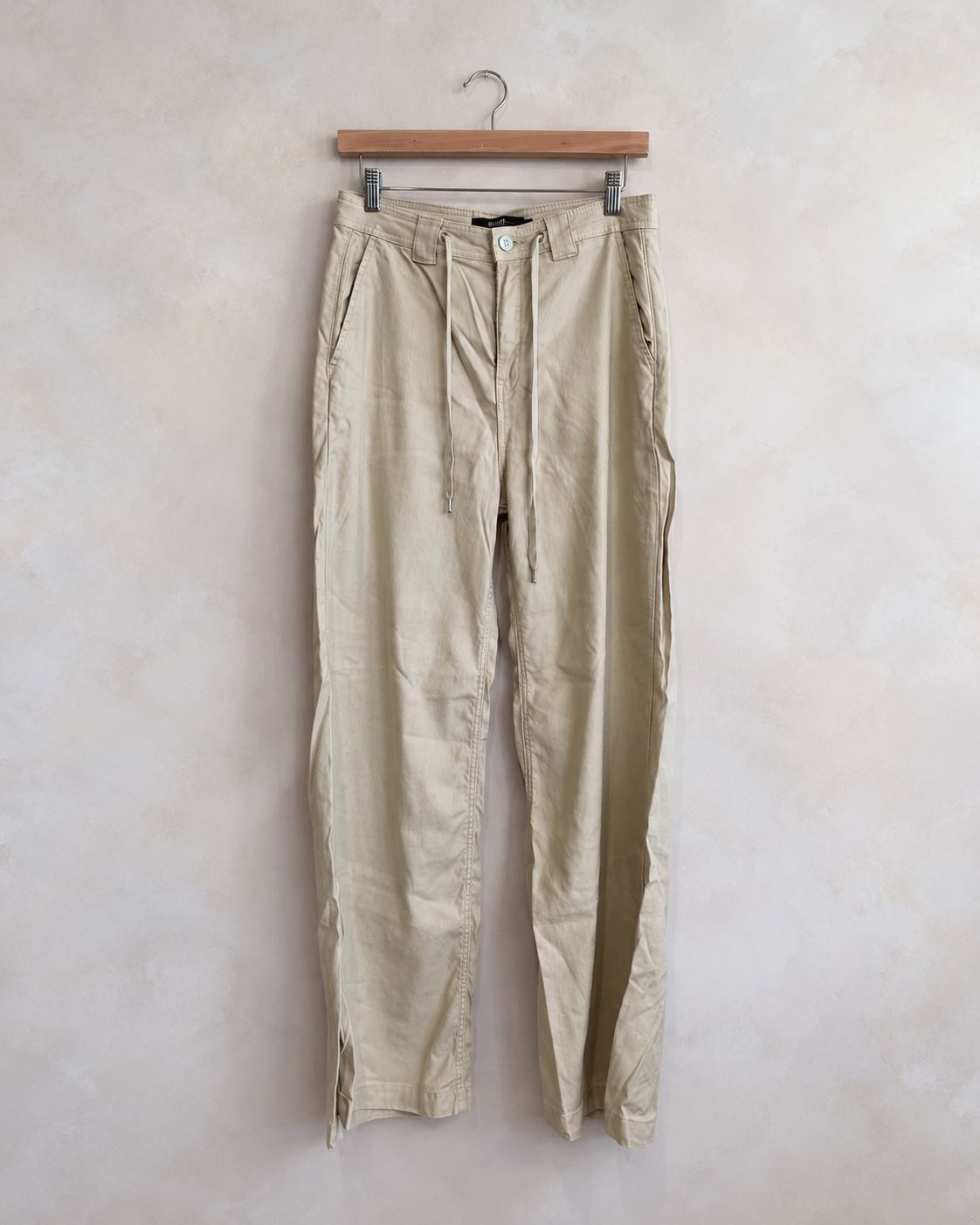Hudson drawstring wide leg twill pants photographed on a wooden hanger against a pale neutral textured wall