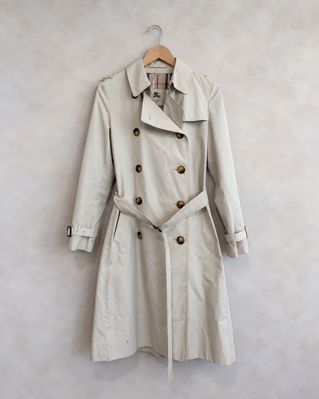 Burberry garment on wooden hanger against pale textured wall