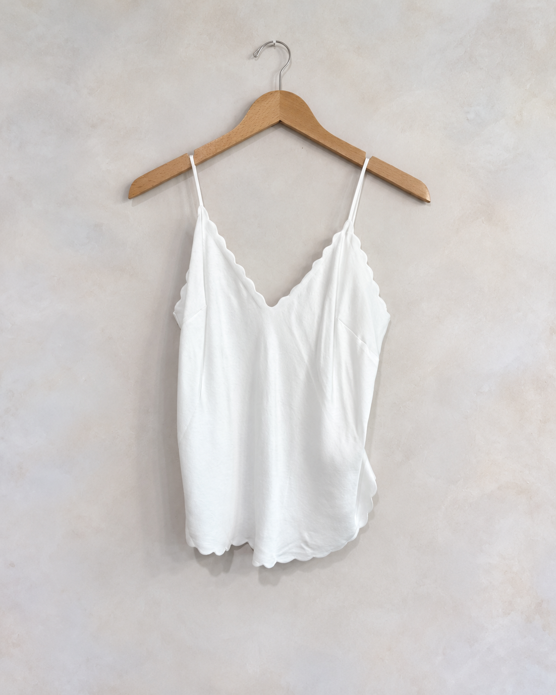 A.L.C Scalloped White Tank, 4 on a wooden hanger against a softly mottled pale wall